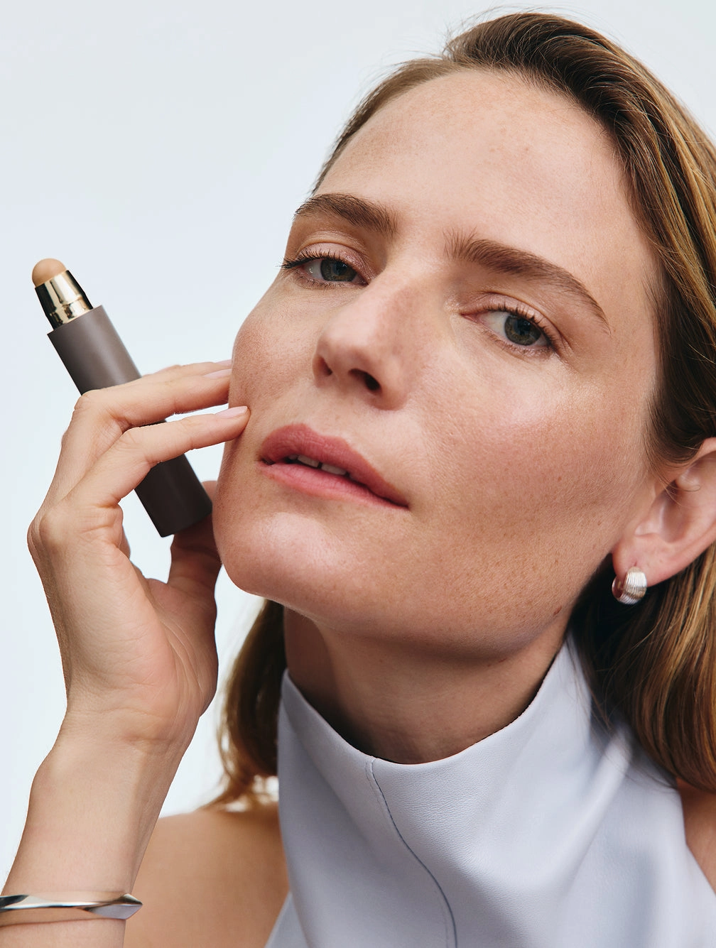 Woman in a white top holding a makeup stick to her cheek