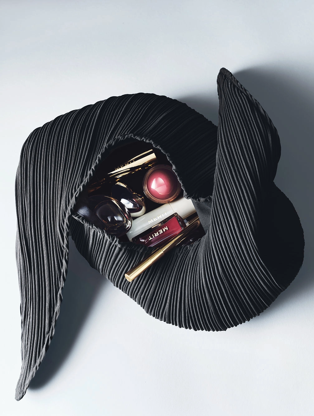 Black pleated Signature Bag open on a grey surface with makeup inside