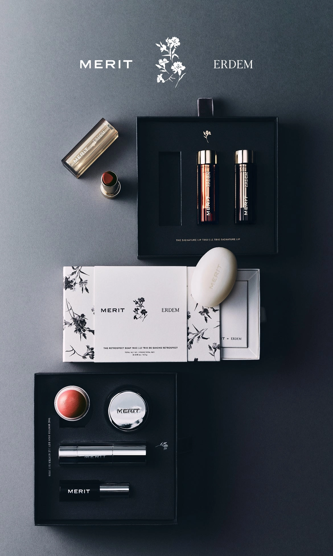Black gift box opened to show a flat lay of MERIT products and printed cards