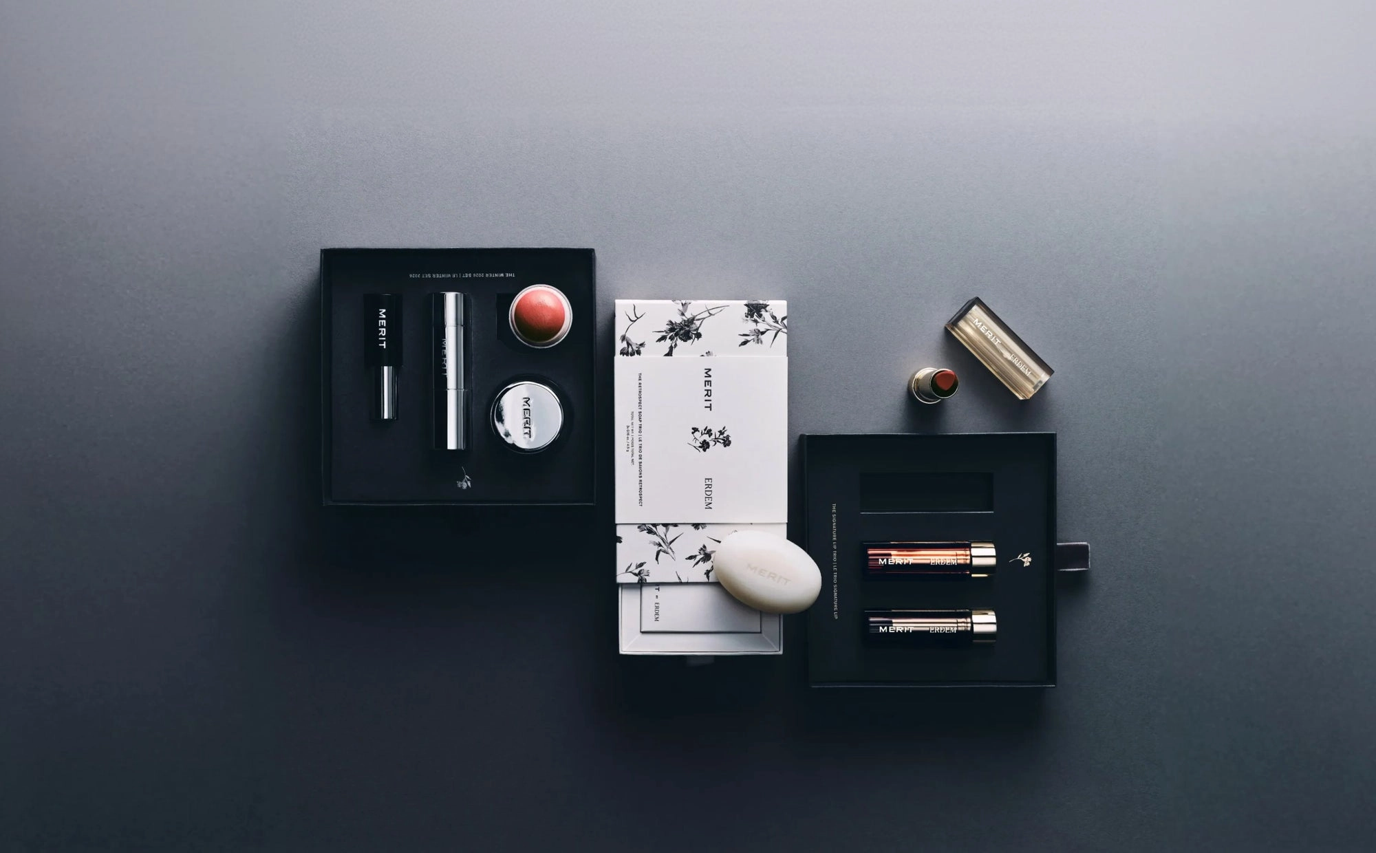 An open MERIT gift box with skincare and makeup laid flat on a dark backdrop
