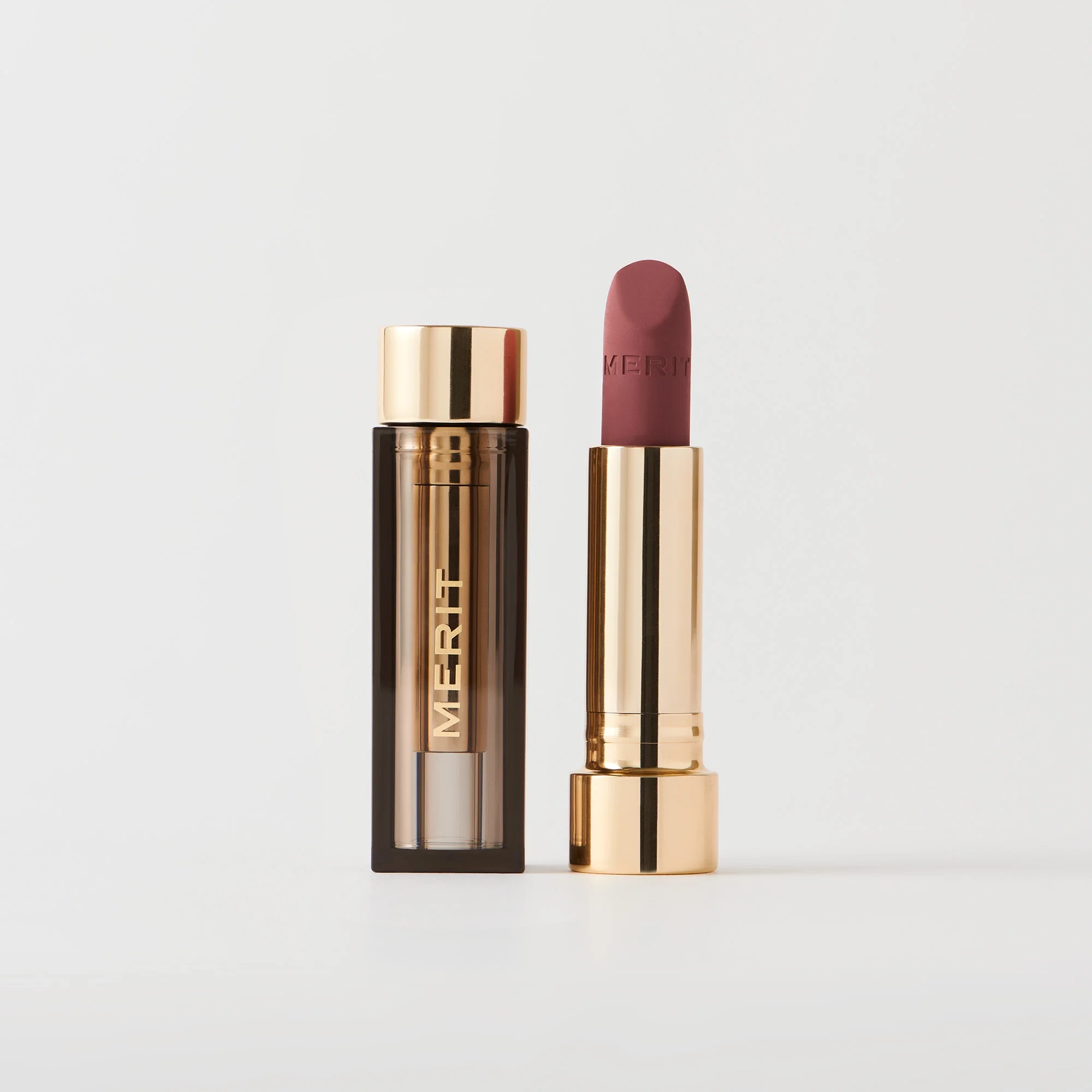 A lipstick with a gold and brown cap next to its open container